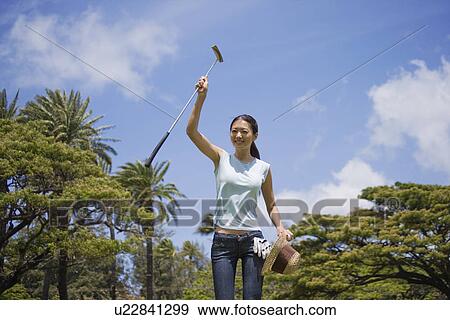 Stock Photo - A woman raising hand by holding golf club and hat. Fotosearch