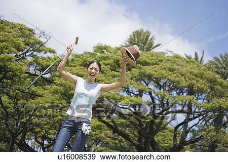Stock Photo - A woman standing with golf club and hat. Fotosearch