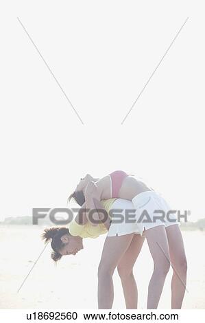 A young woman bends and carries her mate on her back while exercising View Large Photo Image Stock Image - A young woman bends and carries her mate on her back while exercising. Fotosearch