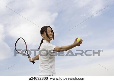 Stock Photograph - A young woman holding a tennis ball and a racquet. Fotosearch
