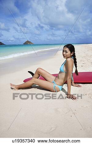 Stock Image - A young woman sitting at beach. Fotosearch