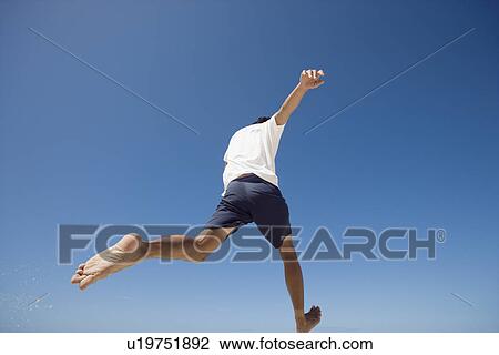Stock Image - Rear view of a man jumping. Fotosearch