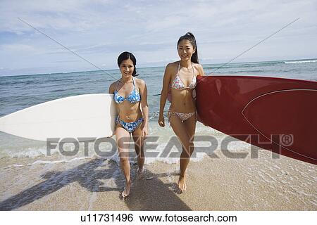 Stock Photograph - Young women walking with surfboards at beach. Fotosearch
