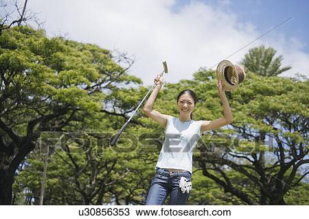 Stock Image - A woman holding golf club and hat. Fotosearch