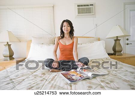 Stock Image - Portrait of young woman sitting on bed. Fotosearch