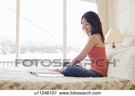 Side view of a young woman sitting on bed View Large Photo Image Stock Photo - Side view of a young woman sitting on bed. Fotosearch