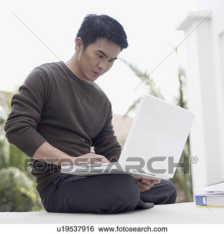 Stock Photograph - Young man sitting on the floor working on a laptop. Fotosearch