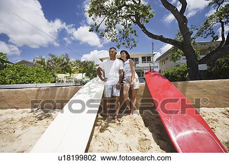 Stock Image - A couple standing near surfboards. Fotosearch