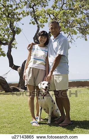 A couple standing with dog in park View Large Photo Image Stock Photography - A couple standing with dog in park. Fotosearch