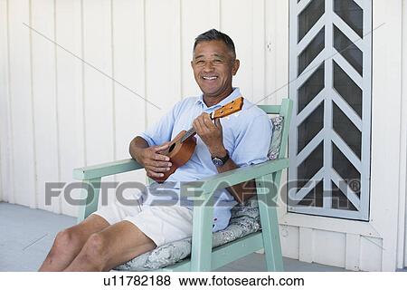 Stock Photo - Mature man playing guitar on chair. Fotosearch