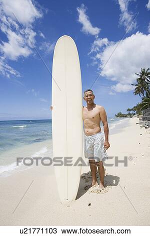 Stock Image - Mature man standing with surfboard on beach. Fotosearch