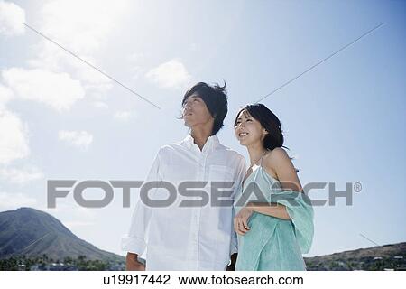 Stock Image - Low angle view of a young couple standing together. Fotosearch