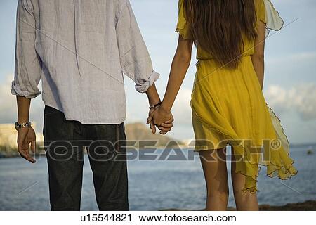 Stock Image - Midsection of a young couple holding hands. Fotosearch