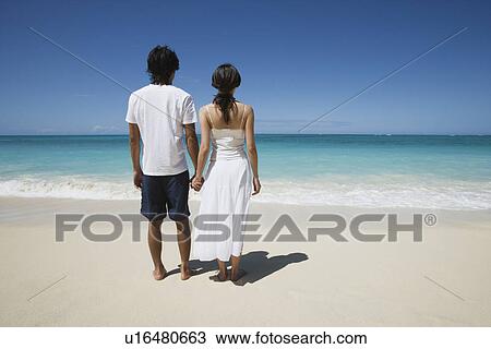 Rear view of a young couple holding hands at beach View Large Photo Image Stock Image - Rear view of a young couple holding hands at beach. Fotosearch
