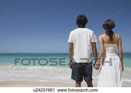 Rear view of a young couple holding hands at beach View Large Photo Image Stock Image - Rear view of a young couple holding hands at beach. Fotosearch