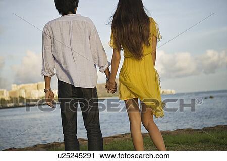 Rear view of a young couple holding hands View Large Photo Image Stock Image - Rear view of a young couple holding hands. Fotosearch