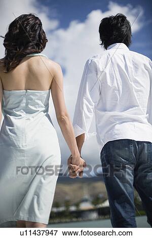 Stock Photo - Rear view of a young couple holding hands. Fotosearch