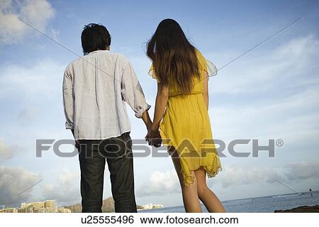 Rear view of a young couple holding hands View Large Photo Image Stock Photograph - Rear view of a young couple holding hands. Fotosearch