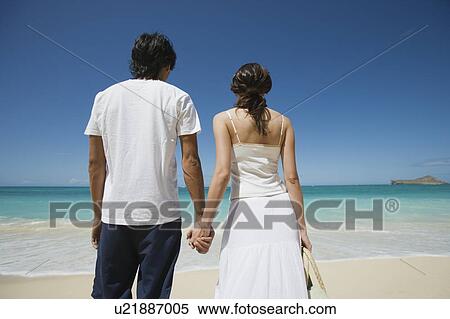 Stock Photography - Rear view of a young couple holding hands at beach. Fotosearch