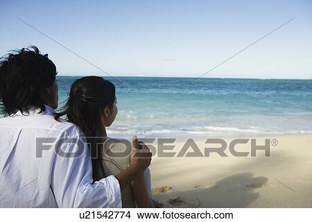 Rear view of a young couple sitting on beach View Large Photo Image Picture - Rear view of a young couple sitting on beach. Fotosearch