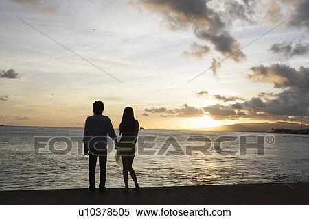 Rear view of a young couple standing at beach View Large Photo Image Stock Photography - Rear view of a young couple standing at beach. Fotosearch