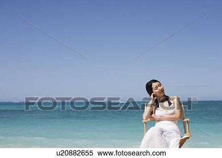Stock Photography - A young woman sitting on chair at beach. Fotosearch