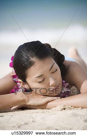 Stock Photo - Close-up of a young woman sleeping on sand at beach. Fotosearch