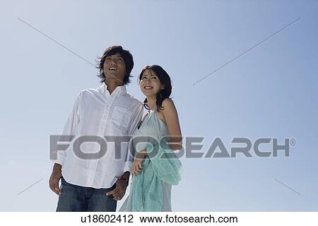 Low angle view of a young couple standing together View Large Photo Image Stock Image - Low angle view of a young couple standing together. Fotosearch