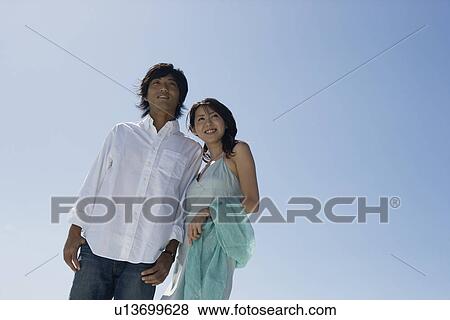 Stock Photo - Low angle view of a young couple standing together. Fotosearch