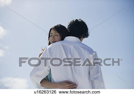 Low angle view of a young couple hugging each other View Large Photo Image Stock Photograph - Low angle view of a young couple hugging each other. Fotosearch