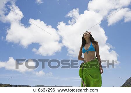 Low angle view of a young woman standing under cloudy sky View Large Photo Image Stock Photograph - Low angle view of a young woman standing under cloudy sky. Fotosearch