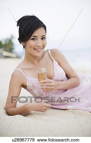 Stock Photo - Portrait of a young woman lying on sand with wineglass. Fotosearch