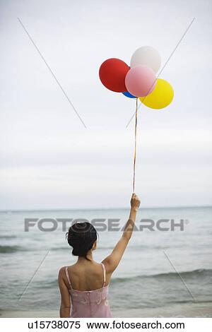 Rear view of a woman holding balloons at beach View Large Photo Image Stock Photography - Rear view of a woman holding balloons at beach. Fotosearch