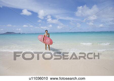 A young woman holding surfboard on beach View Large Photo Image Stock Image - A young woman holding surfboard on beach. Fotosearch