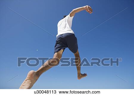 Stock Image - Rear view of a man jumping. Fotosearch
