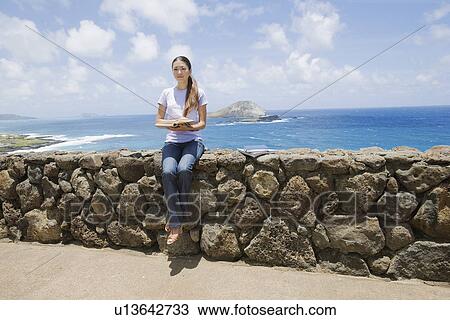View of a young woman sitting on rock with book View Large Photo Image Stock Image - View of a young woman sitting on rock with book. Fotosearch
