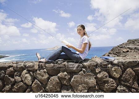 View of a young woman sitting on rock with book View Large Photo Image Stock Photography - View of a young woman sitting on rock with book. Fotosearch
