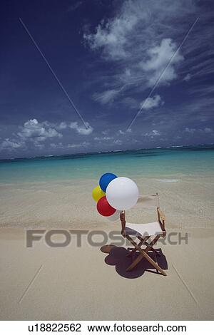 Stock Image - View of air balloons on wooden chair at beach. Fotosearch