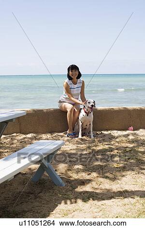 Picture - A woman sitting with dog near sea. Fotosearch