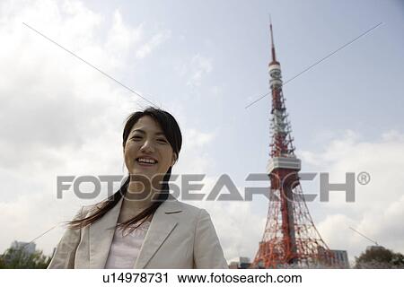 Stock Image - Low angle view of a smiling young woman with tower in background. Fotosearch