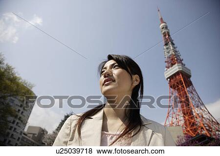 Stock Photo - Low angle view of a young woman with tower in background. Fotosearch