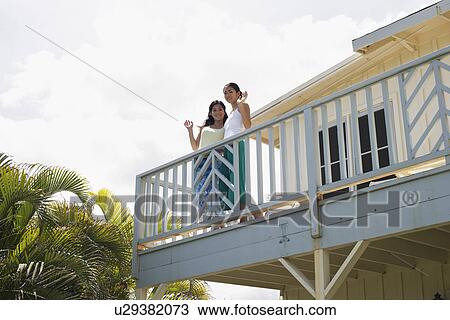 Stock Image - Low angle view of young women standing on balcony. Fotosearch