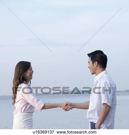 Stock Photo - Side profile of a mid adult man and a mid adult woman shaking hands. Fotosearch