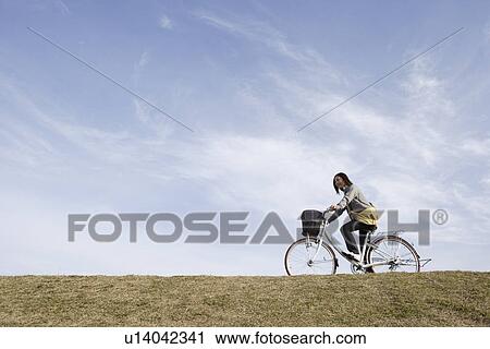 Stock Image - View of a young woman riding a bicycle. Fotosearch