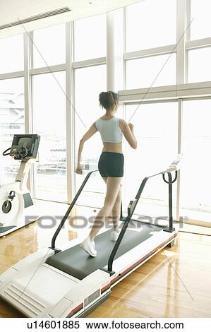 Stock Photography - A young woman jogs on a walker as she exercises in a well equipped gym. Fotosearch