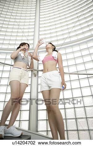 Two young women take a break from exercise as they drink water while standing on the stairs View Large Photo Image Stock Image - Two young women take a break from exercise as they drink water while standing on the stairs. Fotosearch