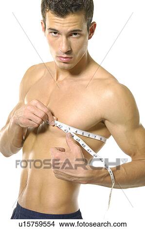 Portrait of a young man measuring his chest with a measuring tape View Large Photo Image Picture - Portrait of a young man measuring his chest with a measuring tape. Fotosearch