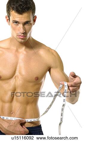 Stock Image - Portrait of a young man measuring his abdomen with a measuring tape. Fotosearch