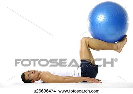 Picture - Portrait of a young man exercising with a fitness ball. Fotosearch