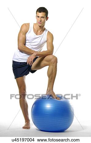 Portrait of a young man standing with his leg on a fitness ball View Large Photo Image Picture - Portrait of a young man standing with his leg on a fitness ball. Fotosearch